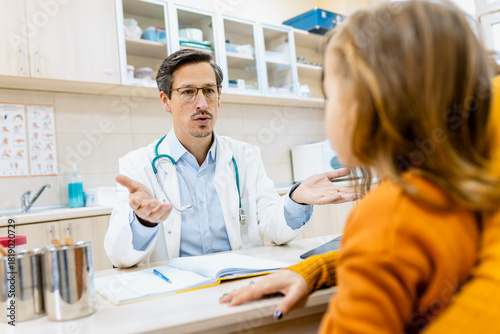 Male pediatrician consulting with a woman and her young child during a medical checkup in clinic.