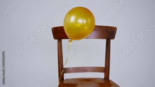 Golden Balloon Resting on a Wooden Chair Against a Neutral Background.