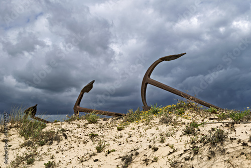 Rusting iron anchors arranged in sand dunes at Praia do Barril, Tavira, Portugal, memorial to tuna fishing heritage,