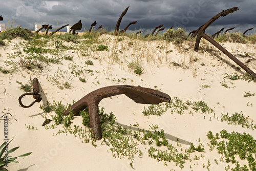 Rusting iron anchors arranged in sand dunes at Praia do Barril, Tavira, Portugal, memorial to tuna fishing heritage,