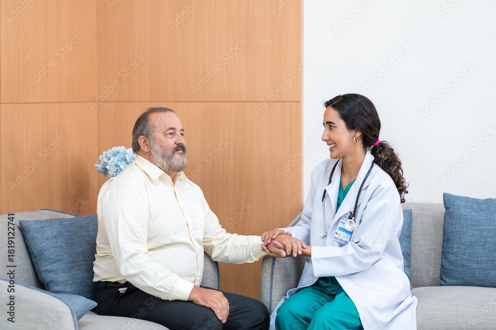Obraz premium Female doctor in white medical coat and patient discussing something, holding his hand and smiling while sitting on sofa. Medicine and health care concept. Doctor and patient.
