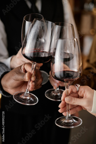 Diverse group of young adult and middle aged hands holding and clinking wine glasses during wine tasting, showing multiethnic participation in social beverage testing event