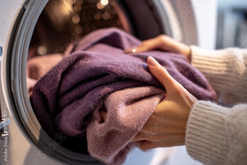 Close-up of hands loading clothes into a washing machine.  Purple garments are being placed inside