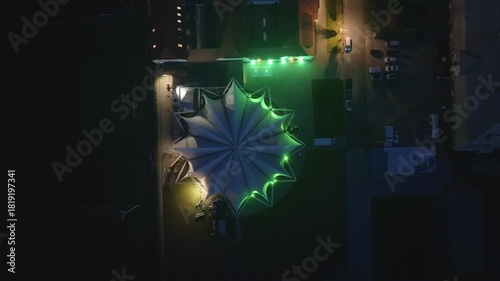 Drone shot of the illuminated tent roof at the Ostra-Dome on the fairgrounds, with green light accents glowing in the night.