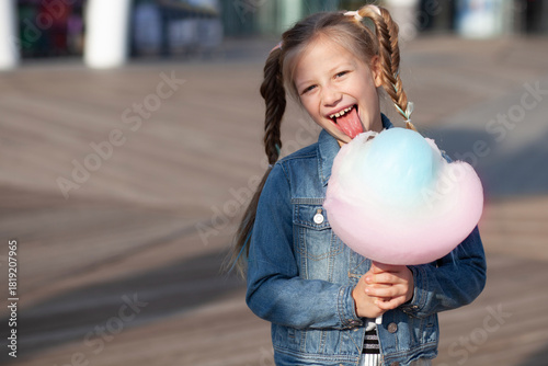 Little blonde girl with colorful braids eating vibrant cotton candy outdoors