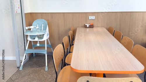 Bright dining area with a long wooden table, multiple chairs and a baby high chair placed nearby in a clean family-friendly eating space