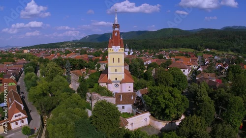 Aerial footage over Cristian village in Brasov county, Transylvania, Romania, with Saxon Evangelical church tower, red-roofed houses and hills on a bright summer day, peaceful rural landscape