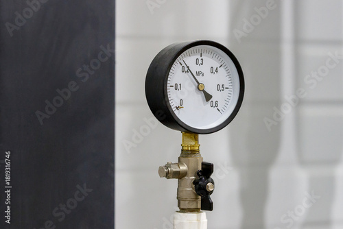 A round pressure gauge in a black case, installed on a pipeline with a valve, shows the pressure