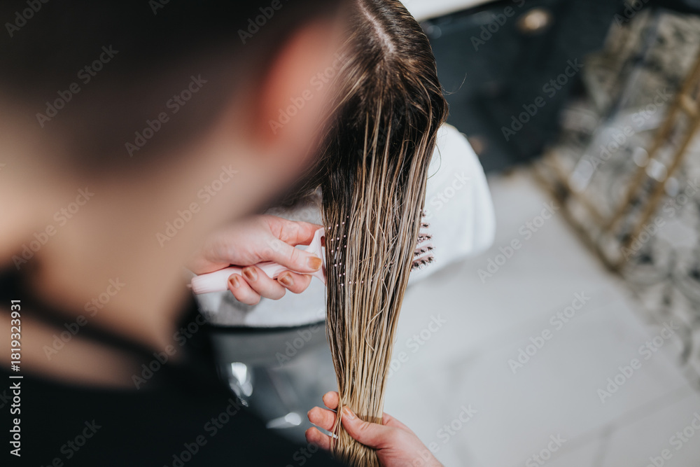 Naklejka premium A stylist focuses on precision while cutting a long blonde client's hair in a clean, modern salon setting. The scene conveys professional grooming and beauty care in a calm environment.