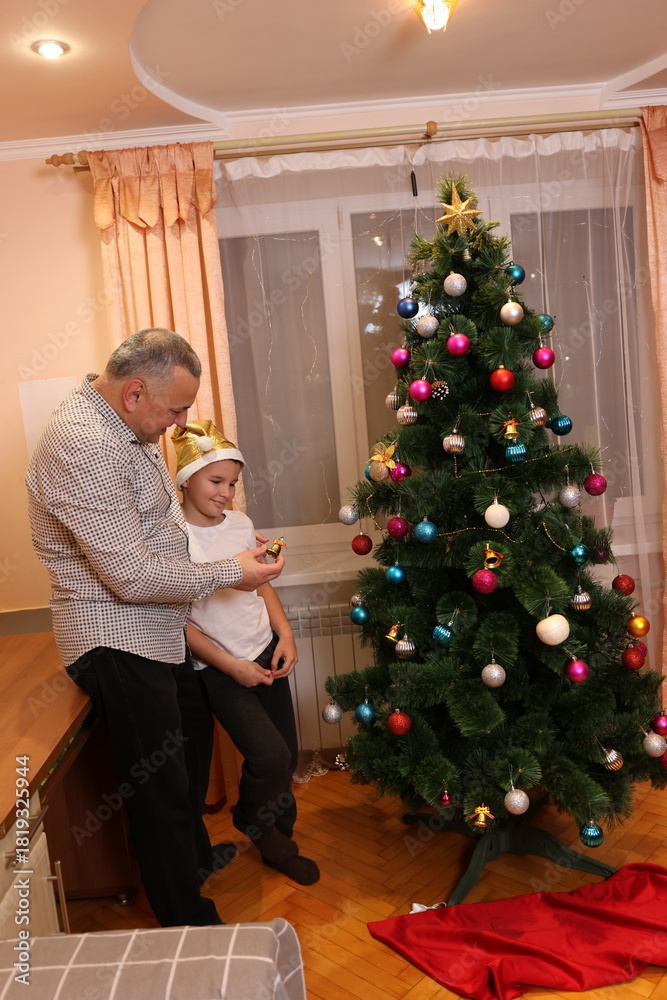 Obraz premium Father and child decorate a Christmas tree at home before the holidays, creating a warm and cozy festive atmosphere.