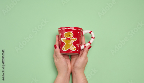 Two female hands holding a red Christmas mug with a gingerbread man on a green background.