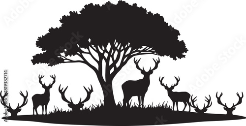 Silhouette of a deer family under a tree in a field of grass.