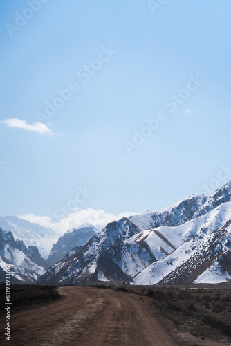 Wallpaper Mural A rough dirt road or track leading forward into a deep valley surrounded by high, steep mountains covered in patches of white snow Torontodigital.ca