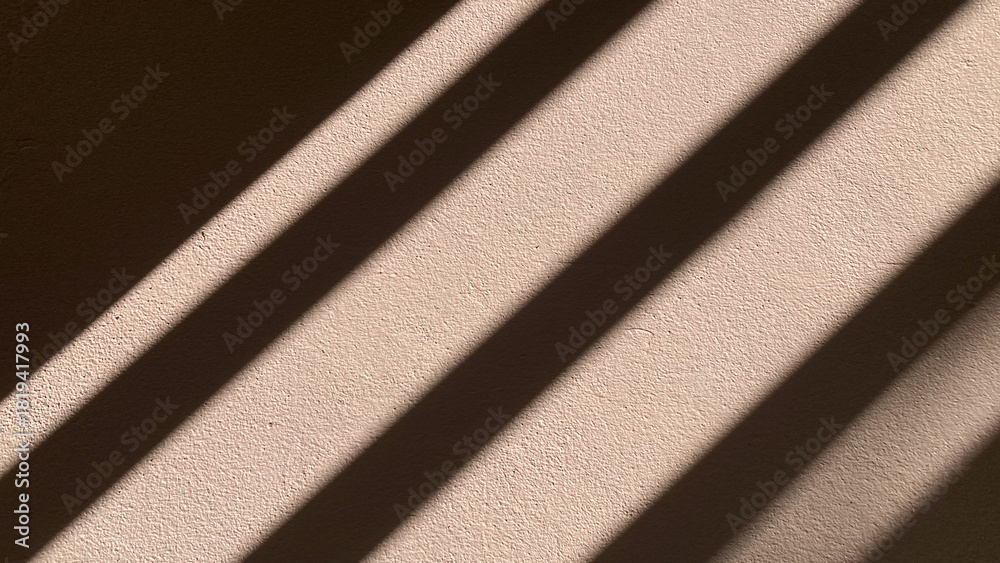 Fototapeta premium Abstract pattern of geometric striped shadows and natural sunlight falling dramatically on a textured white concrete wall background with empty copy space.