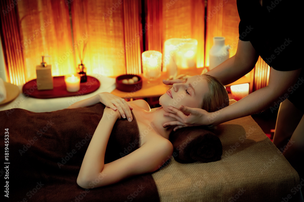 © InfiniteFlow - Caucasian woman enjoying relaxing anti-stress head massage and pampering facial beauty skin recreation leisure in warm candle lighting ambient salon spa in luxury resort or hotel. Quiescent