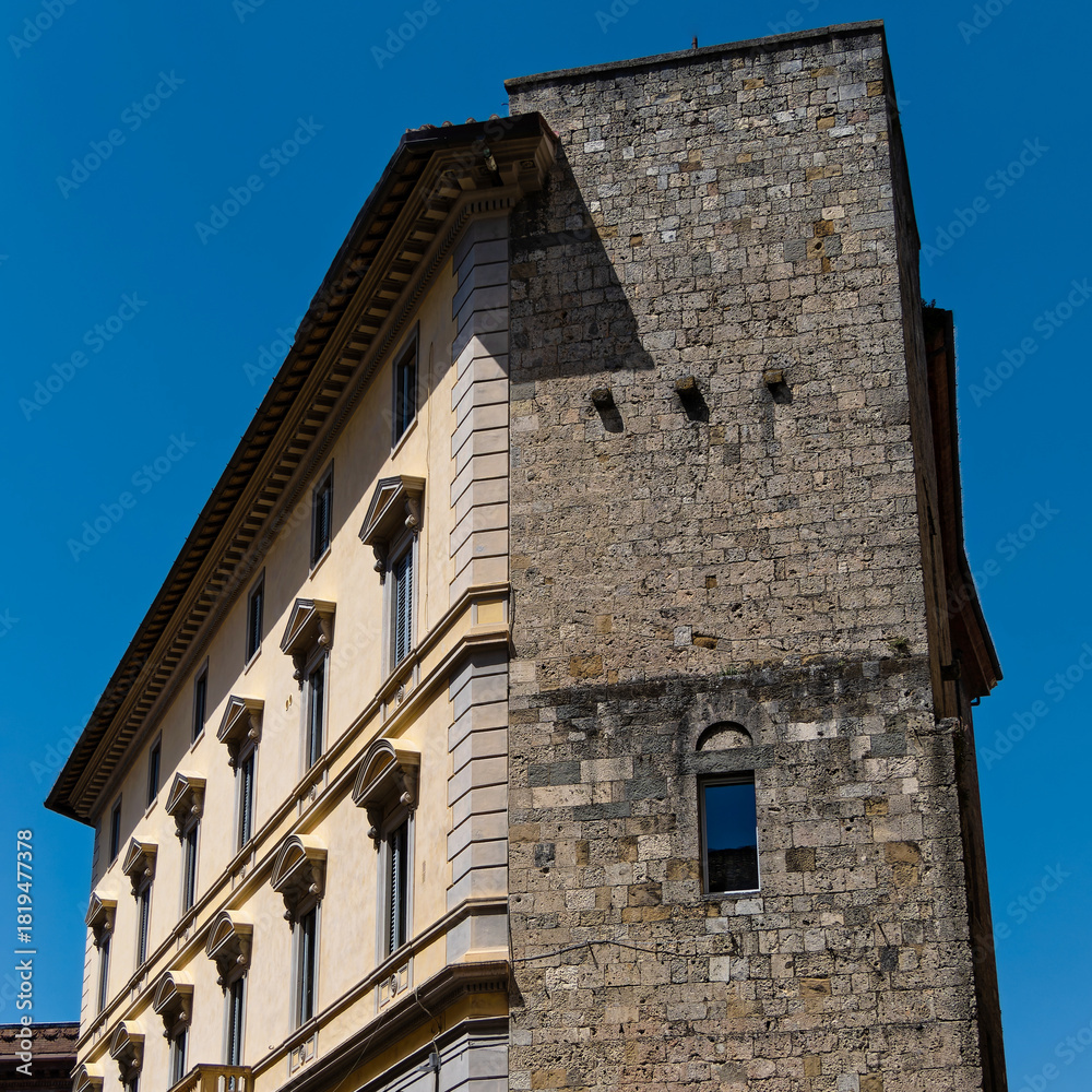 Obraz premium An elegant residential building in Siena, Tuscany,Italy, stands gracefully with yellow and white facade, arched windows, and intricate stonework, complementing the city's charm beneath clear blue sky.