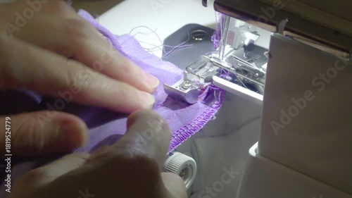 Sewing purple fabric edge on a serger machine in home studio during the afternoon