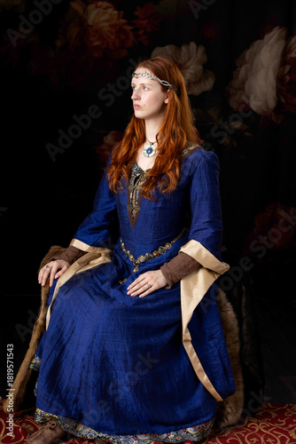 A Medieval or high fantasy woman wearing a blue silk dress and sitting on a chair covered with furs