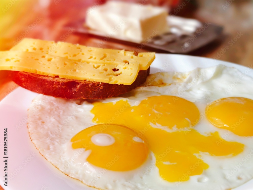 Fototapeta premium Freshly prepared scrambled eggs with the addition of grated cheese on a white plate. The dish is decorated with greens and served with a piece of whole grain bread and cherry tomatoes..