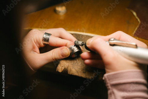 Jewelry ring hands polishing workshop tool craftsman metal working on a wooden bench using a rotary tool to refine a silver ring closeup showing skill manual craft and delicate finishing details