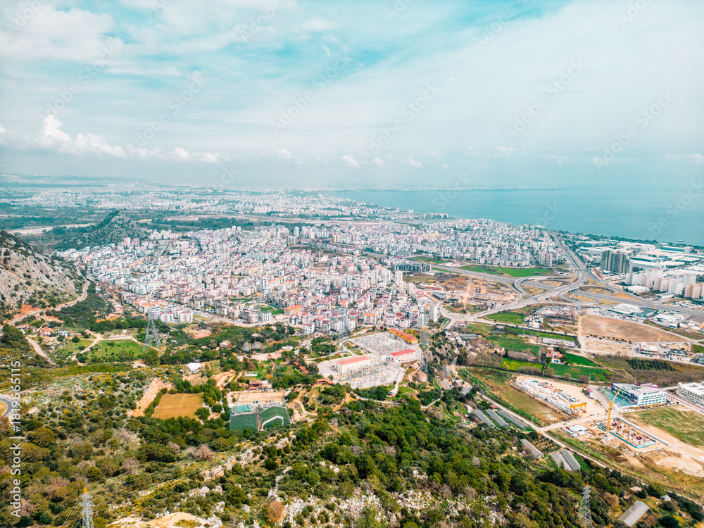 Obraz premium A bright aerial panorama of a coastal city blending urban density with open landscapes and the sea, captured in soft natural light