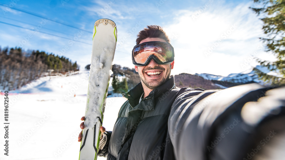 Fototapeta premium Happy skier taking selfie pic with smart cell phone device outside - Young man having fun on weekend activity in ski resort vacation - Winter sport concept