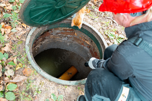A worker inspects an open manhole with a sewer pipe. Maintenance of underground infrastructure. Septic tank cleaning