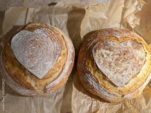 Two round sourdough loaves with heart shapes skillfully scored into the golden brown crust. 