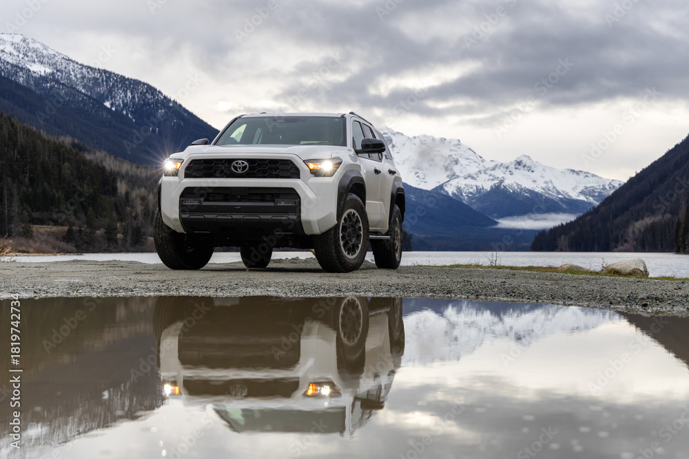 Naklejka premium White Toyota 4Runner SUV By Mountain Lake With Reflections, Snowy Peaks, And Overcast Sky