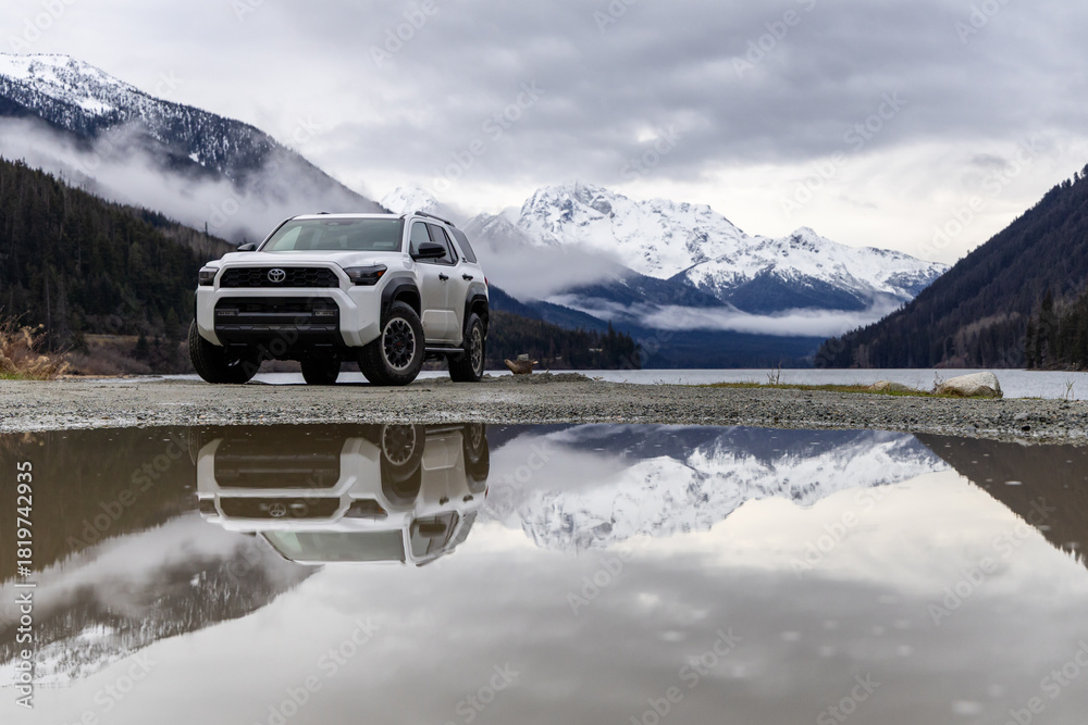 Obraz premium White Toyota 4Runner SUV By Mountain Lake With Reflections, Snowy Peaks, And Overcast Sky