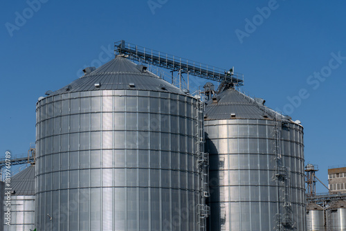 Schilderij op canvas Steel grain silos stand tall against a clear blue sky in an agricultural setting
