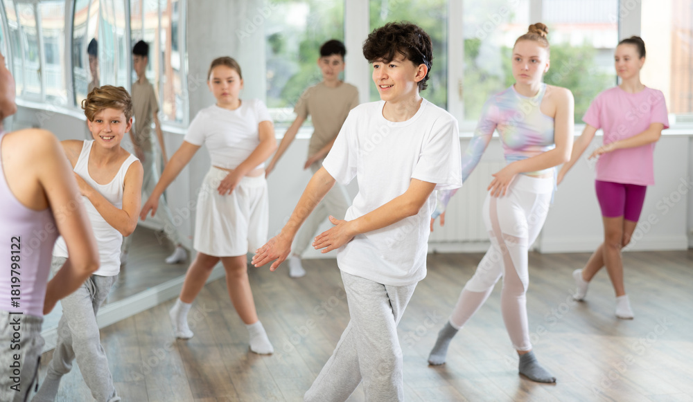 Naklejka premium Male boy student repeats movements of unrecognizable teacher during group modern dance class. Hobbies, active pastime, additional extracurricular activities for children and teenagers