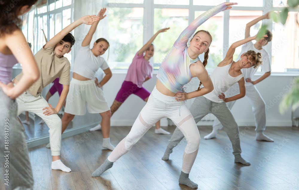 Fototapeta premium Group of boys and girls with teacher doing warm-up exercises before dancing in studio