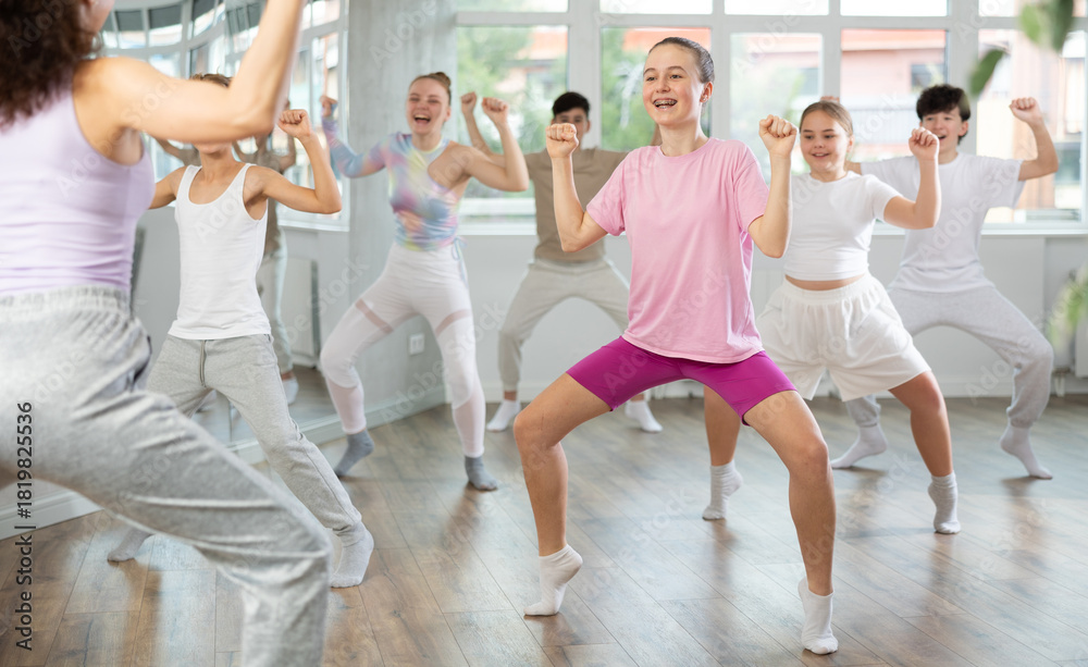 Fototapeta premium Female teacher performs choreographic exercises and teaches energetic mobile social house dance together with teenagers