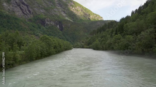 A still view of the Jostedøla River in Gaupne, Norway, with steam rising from the water and verdant mountain slopes on either side. Peaceful Nordic nature in a serene and picturesque landscape