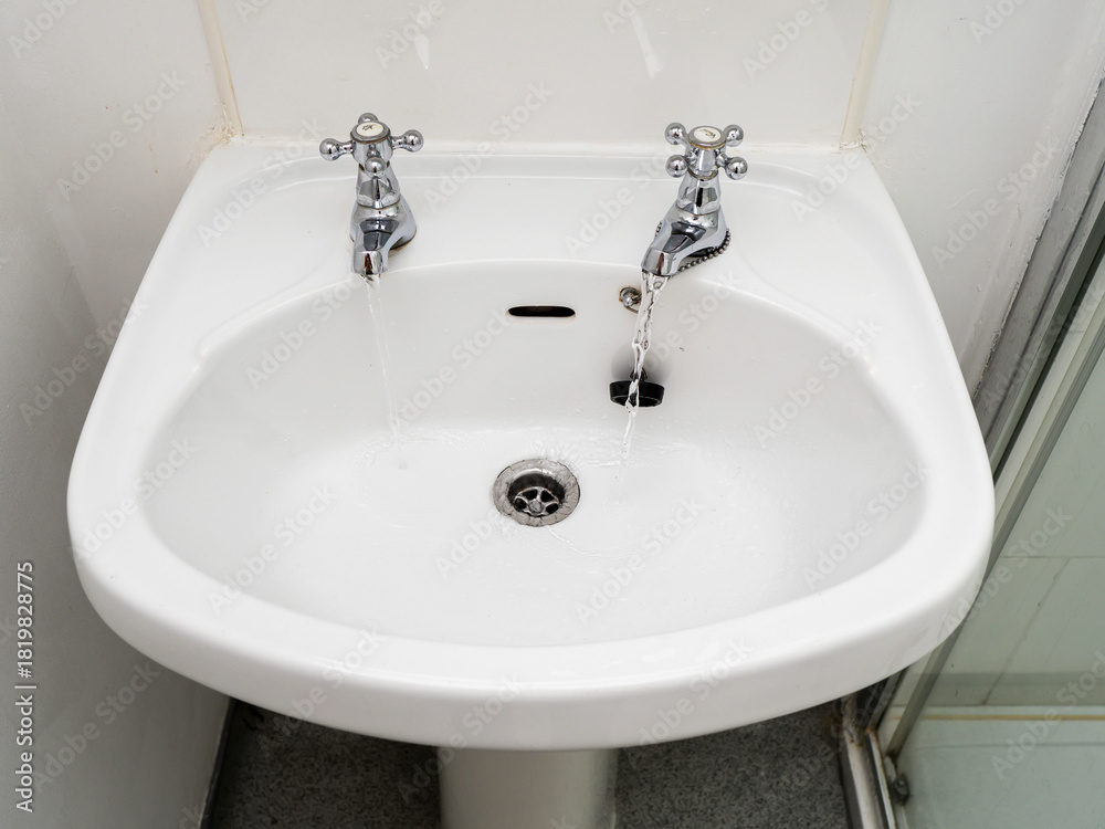 Fototapeta premium A white British style sink with two separate faucets and a drain. The sink is in a bathroom.