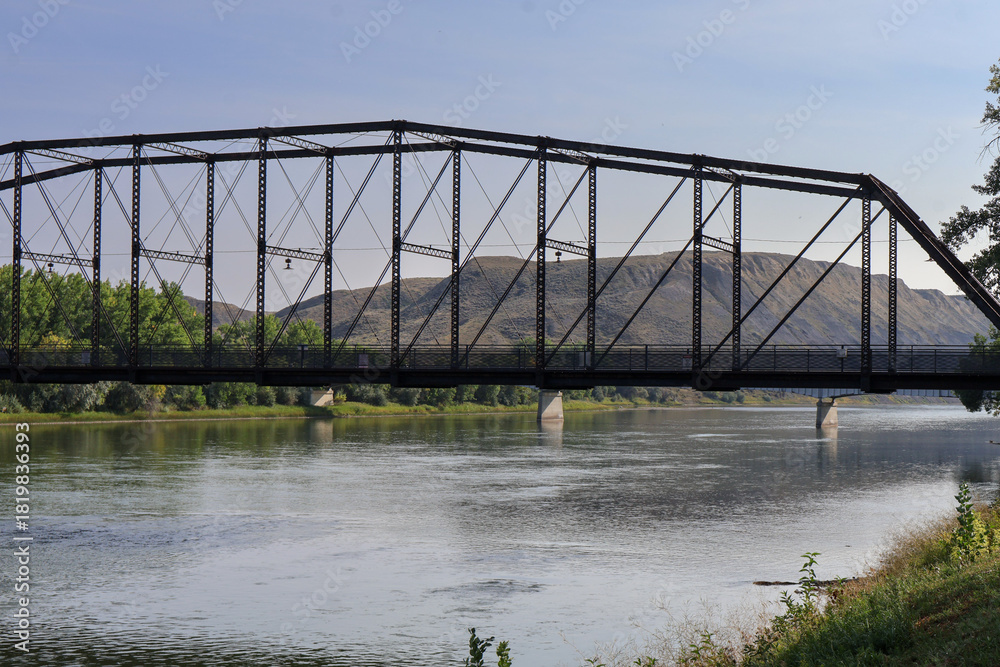 Fototapeta premium Close-up view of historic steel truss bridge over calm river with dry hills in background