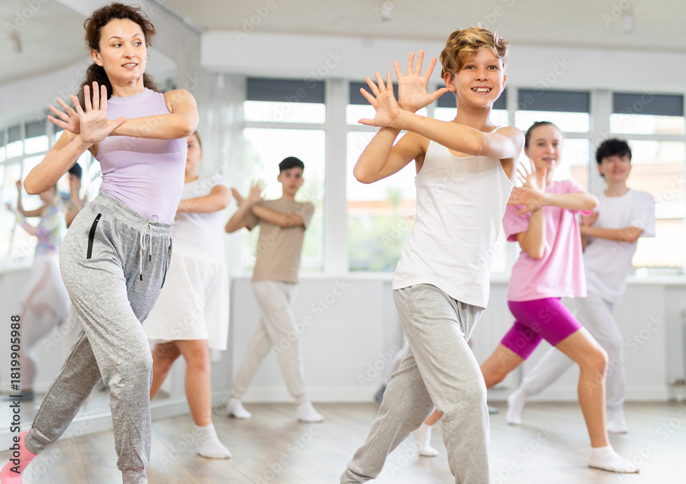 Naklejka premium Teenage boys and girl rehearse hip hop dance performance together with female instructor. Preparing for performance of choreographic team, practicing skills, repeating exercises