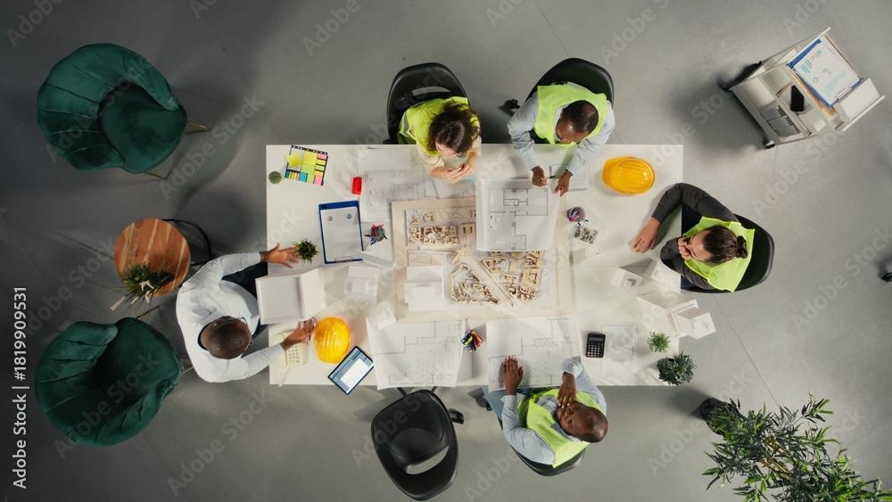 Obraz premium Top down view of property developers and architects in meeting reviewing blueprints and structural designs. Team discusses project approval and city planning for housing growth.