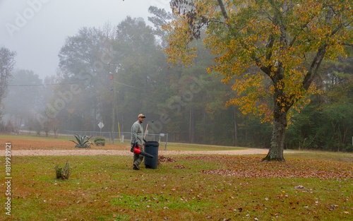 A person is seen racking and blowing leaves in a yard on a foggy day. The autumn leaves are scattered on the ground, adding to the serene atmosphere.