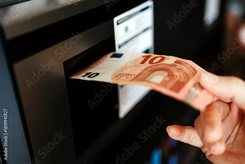 Hand inserting a ten euro banknote into an automated cash machine, showcasing the transaction process in a modern financial environment with technology and convenience