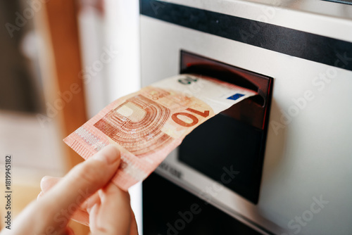 Hand holding a 10 euro banknote as it is being inserted into a cash machine, showcasing the process of withdrawing money in a modern financial environment