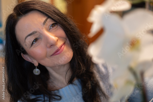 Woman with dark hair gently caring for houseplants, showcasing her love for nature and the environment, surrounded by vibrant greenery and blooming flowers