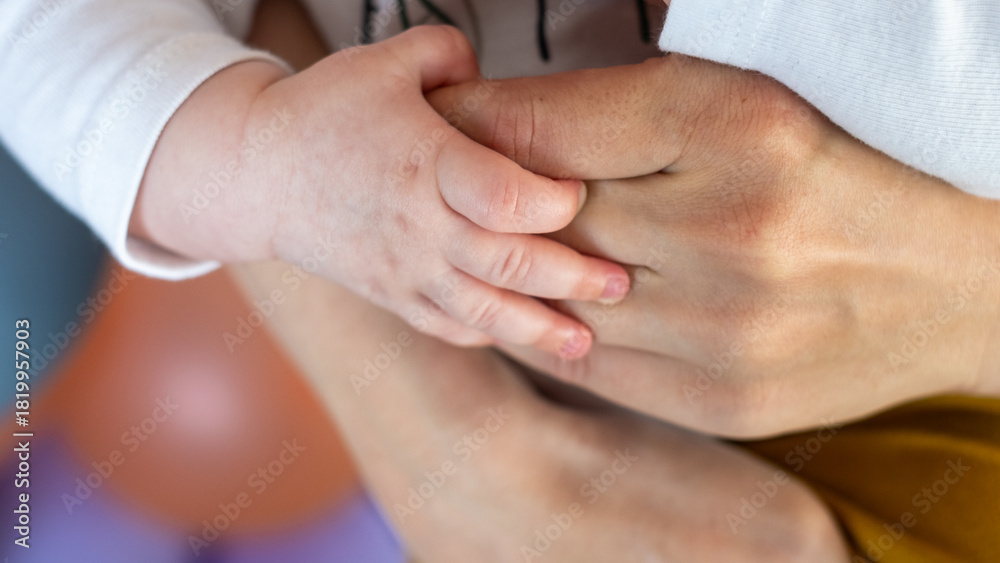 Fototapeta premium Close-up of a child's hand grasping an adult's hand, symbolizing the bond of family, love, and the passage of time between generations in a warm, colorful setting