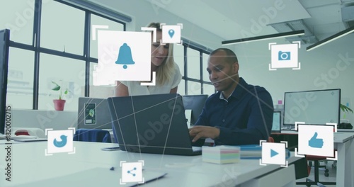 Collaborating coworkers in business attire leaning over laptop at office with digital icons