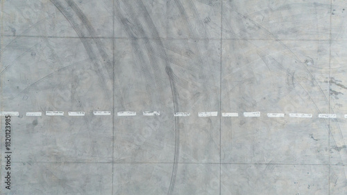 Top down aerial texture of a grey concrete parking lot with white lines and tire marks creating an urban industrial background