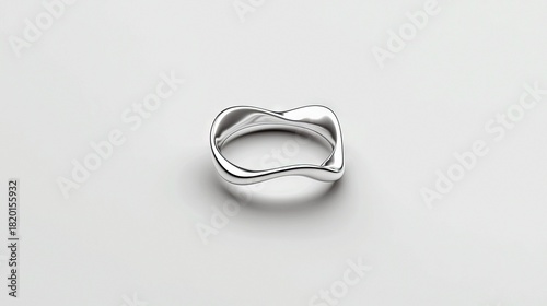 A single, modern silver ring with a fluid, wavy design rests on a seamless white surface, illuminated by soft studio light.