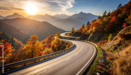 A beautiful winding mountain road during sunset, flanked by vibrant autumn foliage. The majestic peaks fade into the hazy distance.