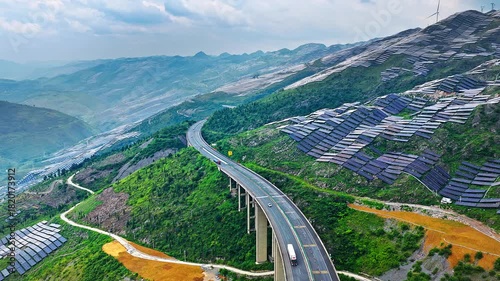  Aerial shot of highway bridge winding through green mountains covered with solar panels energy farm in China