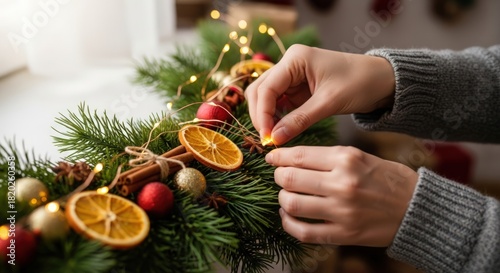 Close-up of hands decorating a Christmas wreath with dried orange slices and ornaments.